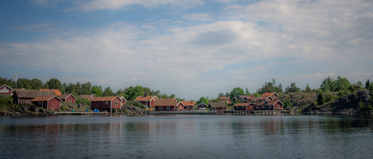Rij rode Zweedse houten huisjes aan de waterrand van Stora Grindö, omgeven door naaldbos en weerspiegeld in het donkere water