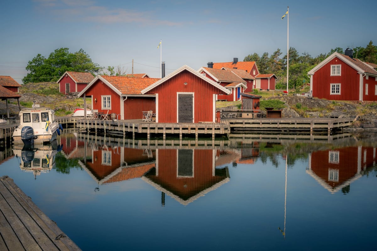 Rode houten huizen van Stora Grindö langs een steiger met een perfecte spiegelende weerspiegeling in het spiegelgladde water