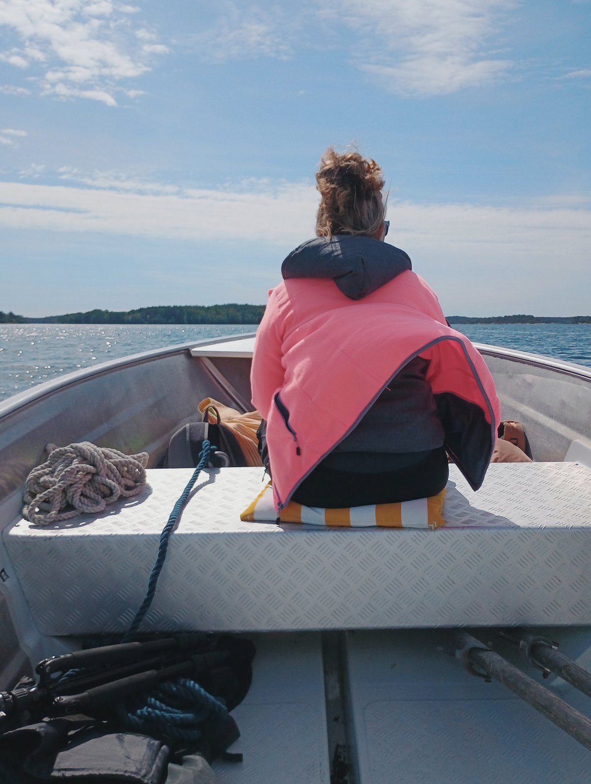 Persoon met roze jack zit op de boeg van een motorboot en kijkt uit over een kalm meer met beboste eilanden aan de horizon.