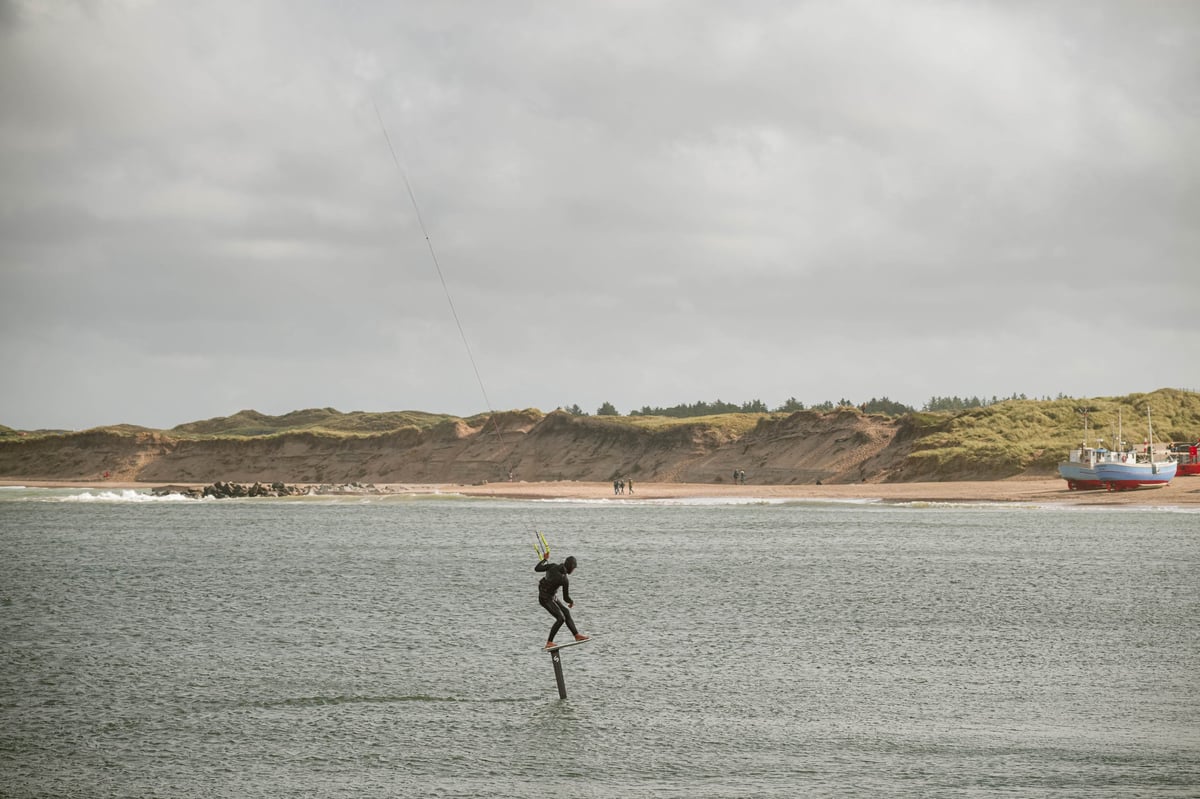 Kitesurfer on hydrofoil board glides above choppy coastal waters.