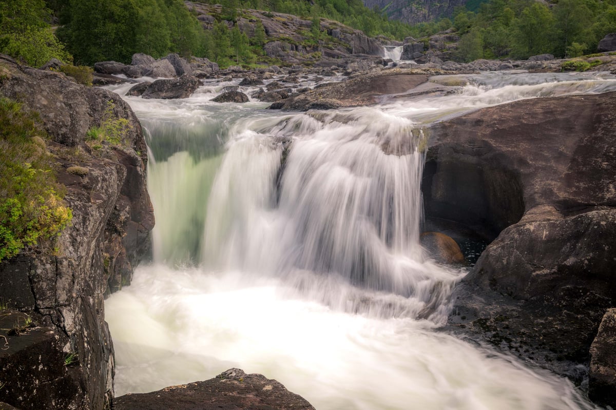 Zijdezachte waterval stroomt tussen mosbegroeide rotsen in een groen Noors berglandschap, lange sluitertijd.