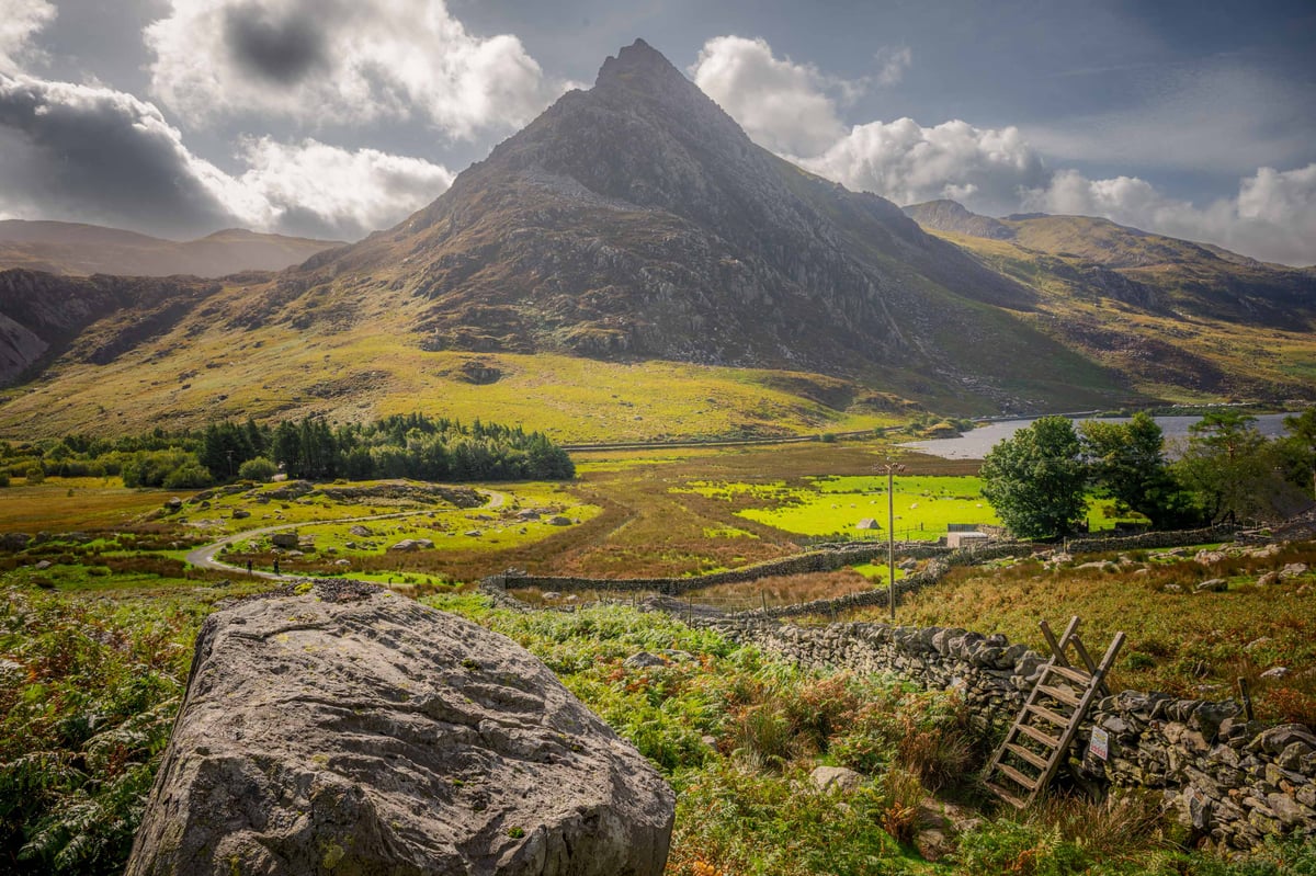 Piramidevormige top van Tryfan boven het dal van Llyn Ogwen, met droge stenen muur en houten stijgbeugel op de voorgrond