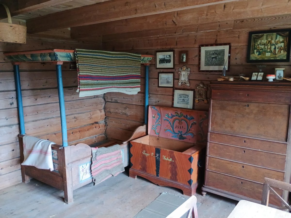 Historische Scandinavische slaapkamer met hemelbed, beschilderde houten kist uit 1888 en ladenkast in een houten boerderijinterieur op Jonegarden