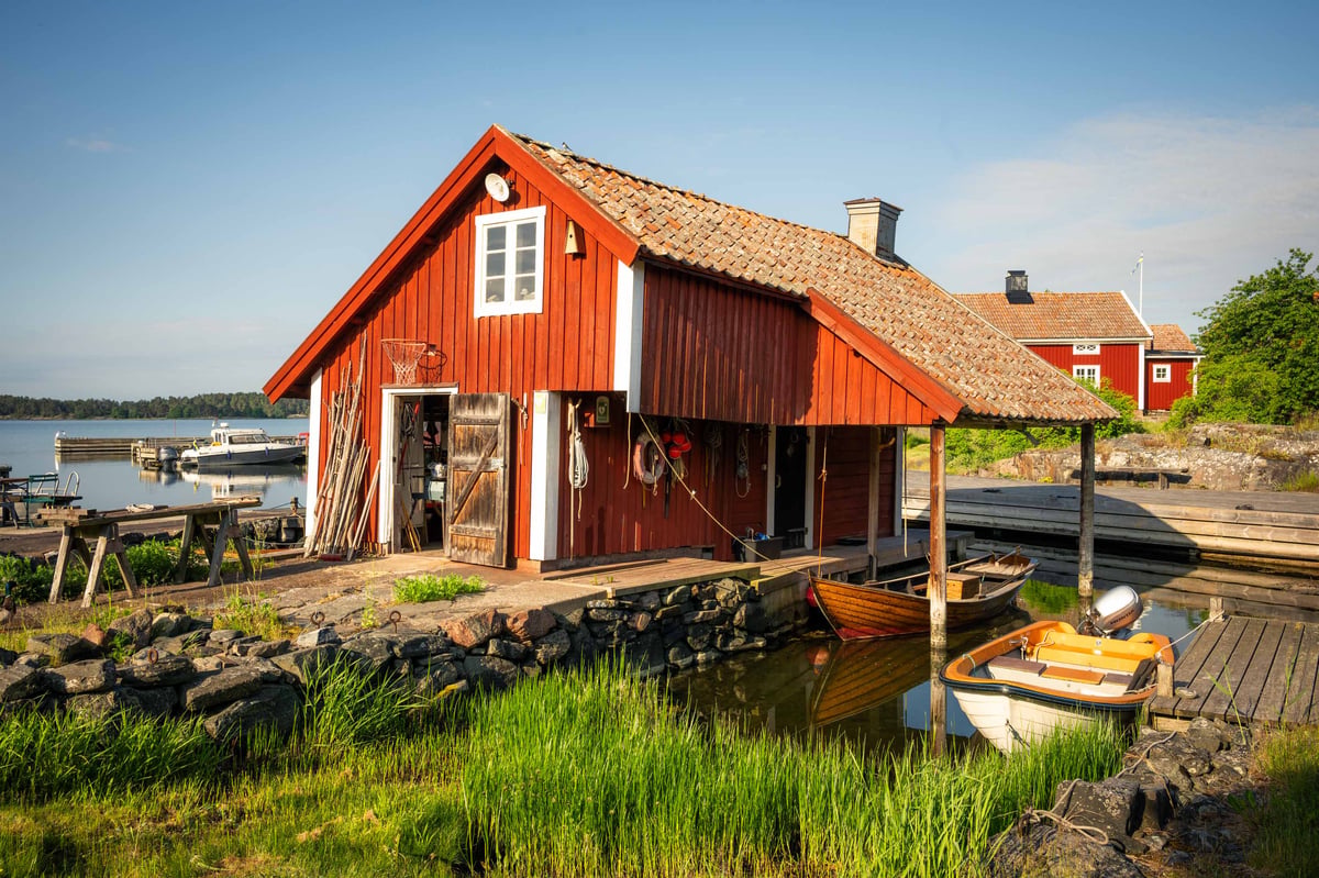 Klassiek rood Zweeds botenhuis bij Loftahammar aan het water met houten steiger en roeibootjes in warm avondlicht