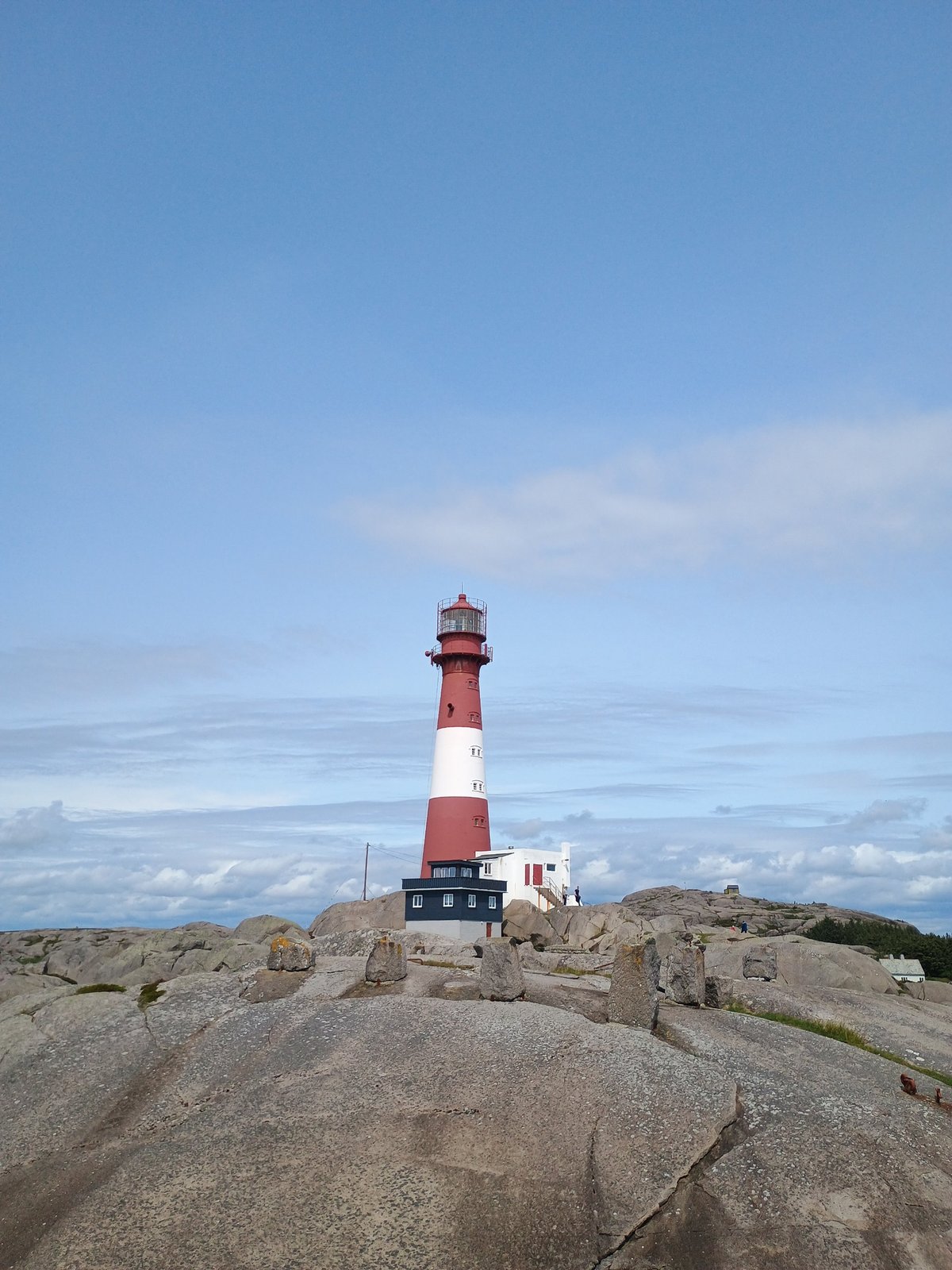 Rode en witte vuurtoren op een kale rotsige kust onder een lichtbewolkte blauwe lucht.