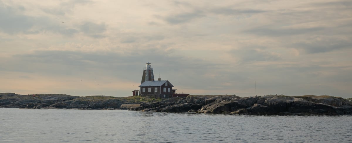 Vuurtoren van Storkläppen met rood bakstenen gebouw op een rotseiland, vanuit het water gefotografeerd bij diffuus avondlicht