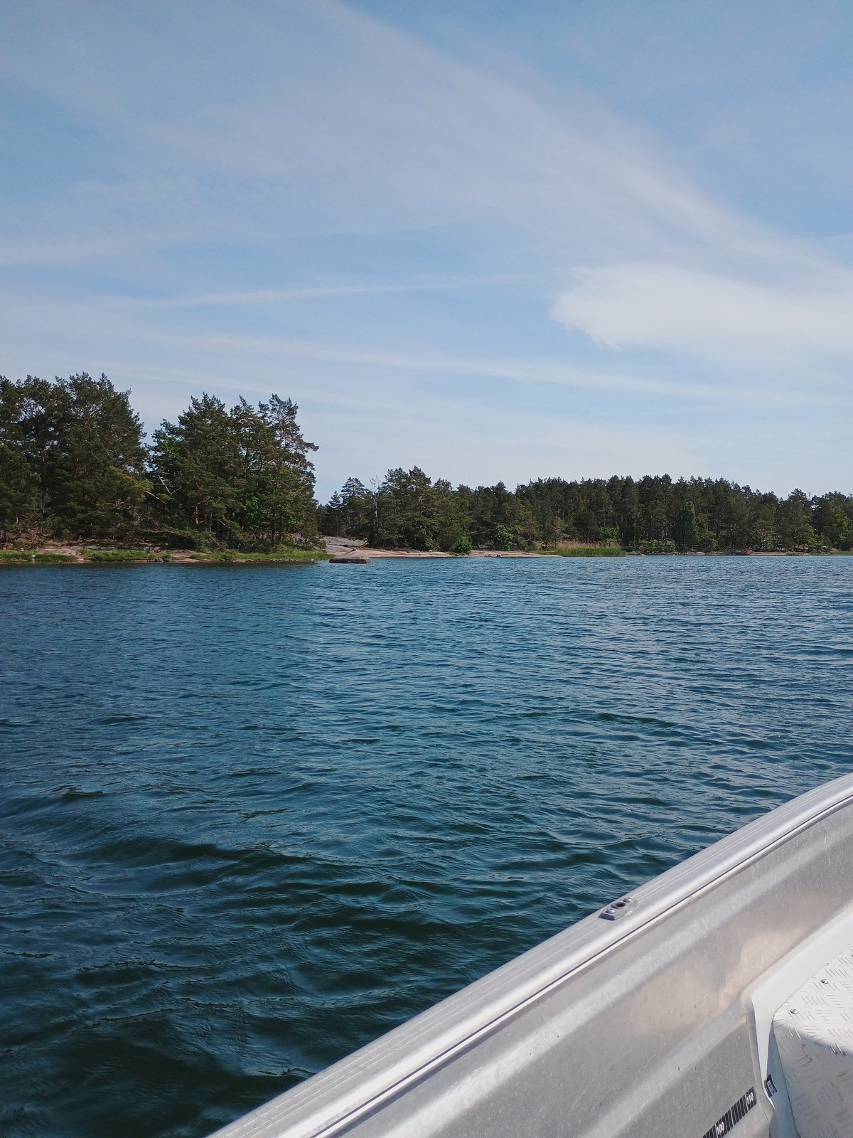 Uitzicht vanuit een motorboot op een Scandinavisch archipel met rotseilandjes en naaldbomen onder een blauwe zomerlucht.