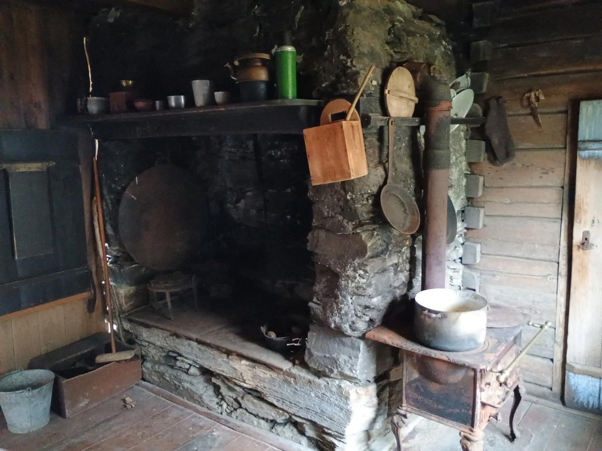 Rustiek interieur van een oude hut met grote stenen haard en gietijzeren kachel omringd door vintage kookgerei op Jonegarden