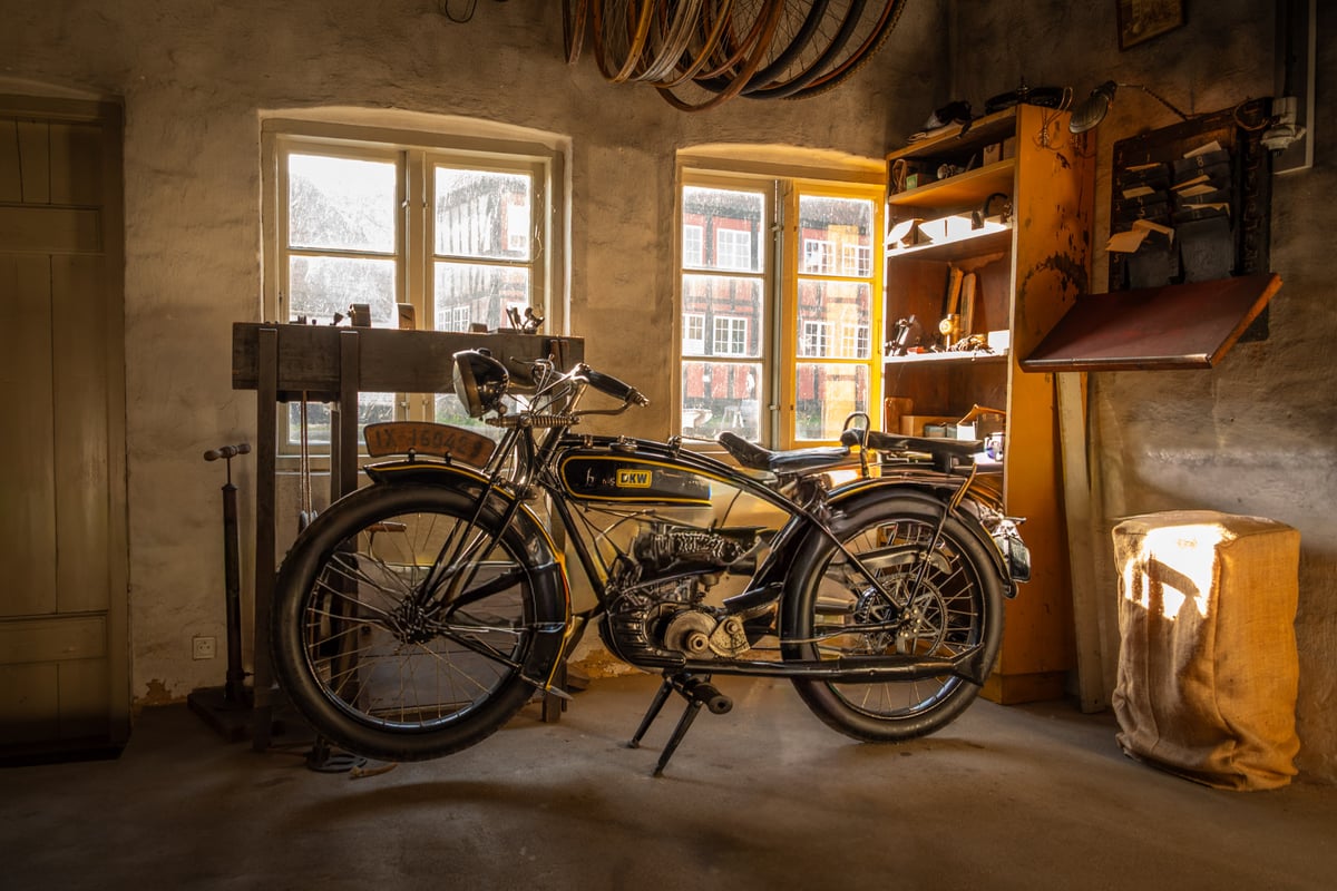 Vintage DKW-motorfiets in een oude werkplaats met warm invallend licht door twee ramen.