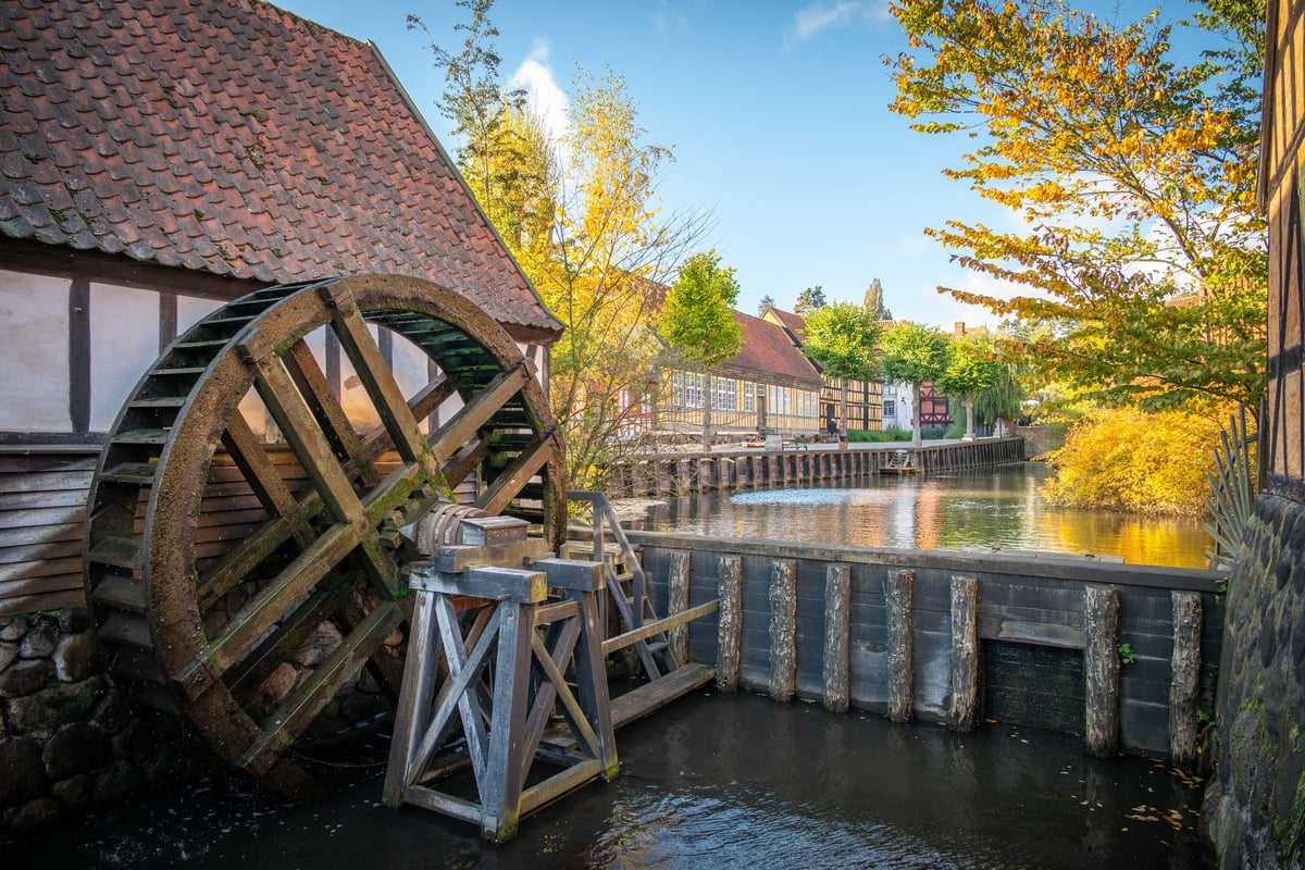 Houten waterrad van een historische molen aan een kanaal in een middeleeuws dorp tijdens de herfst.