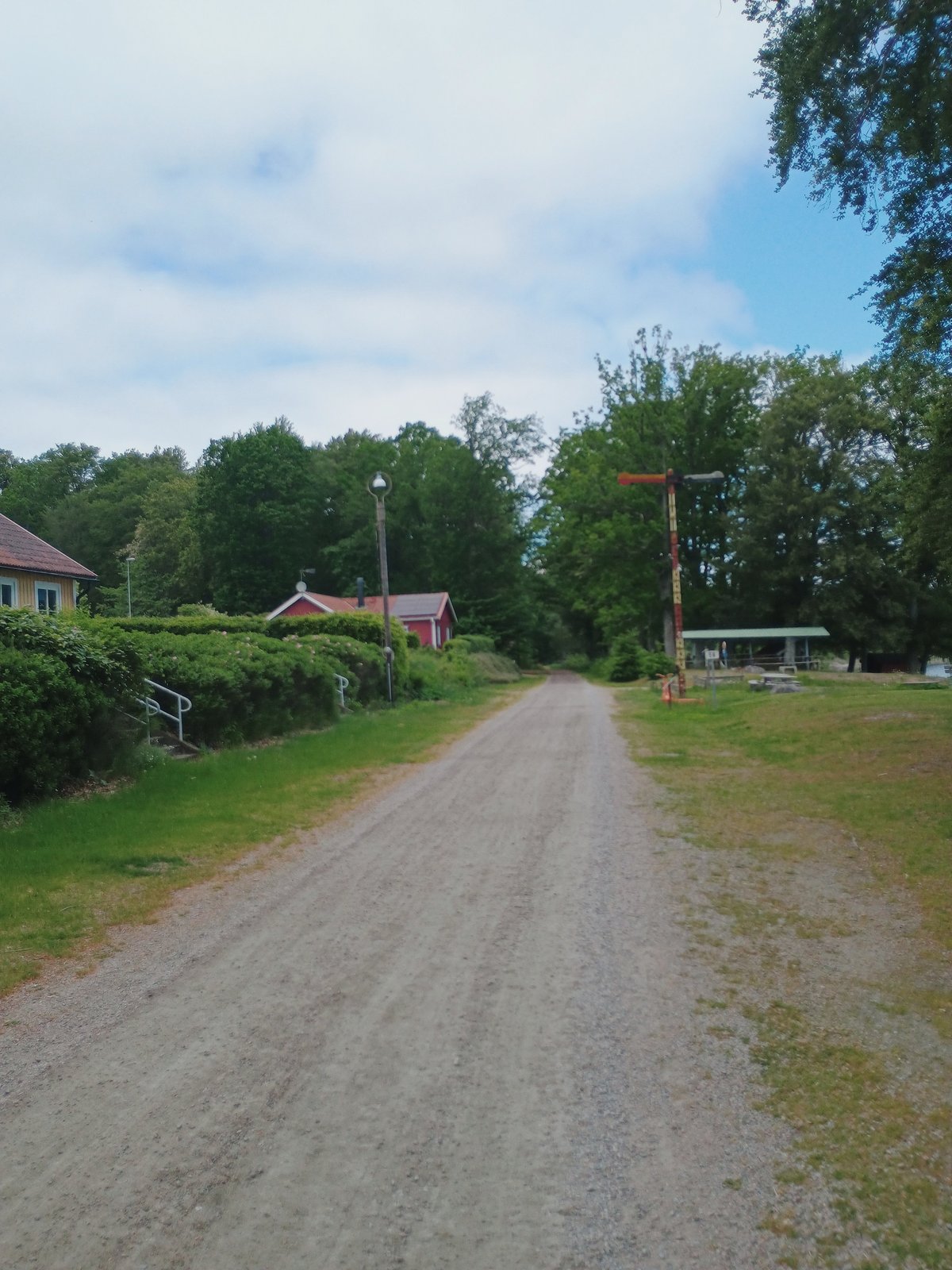 Een smalle grindweg tussen groene heggen en rode houten huisjes in een Scandinavisch dorpje op een bewolkte zomerdag.