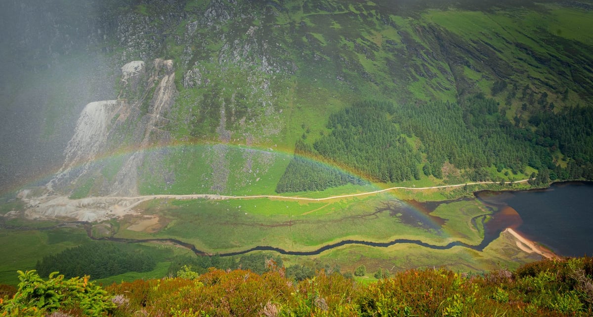 Regenboog over Upper Lake Glendalough met berghellingen op de achtergrond