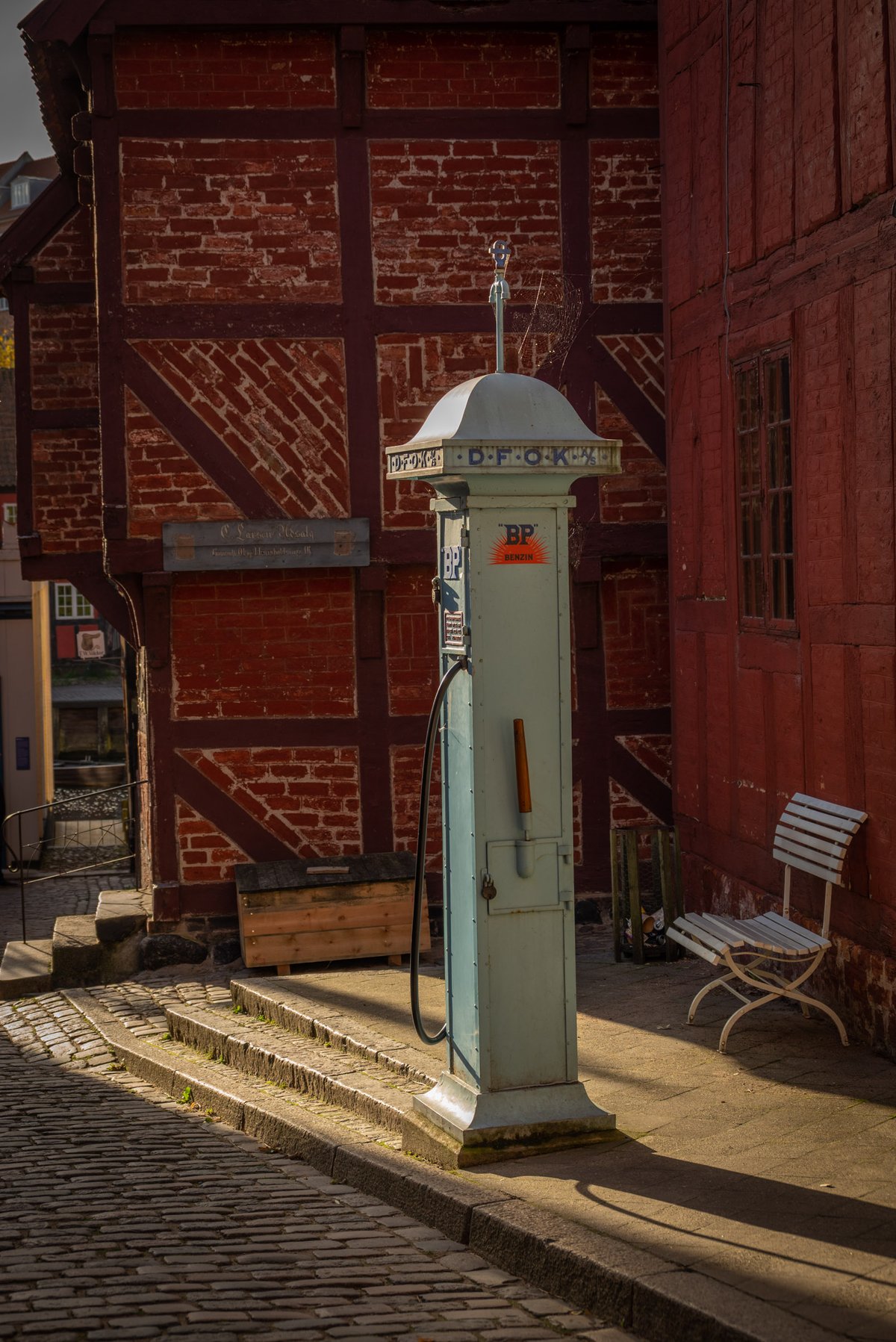 Vintage lichtblauwe BP-benzinepomp op kasseienplein voor een rood vakwerkhuis in een historische Europese stad.