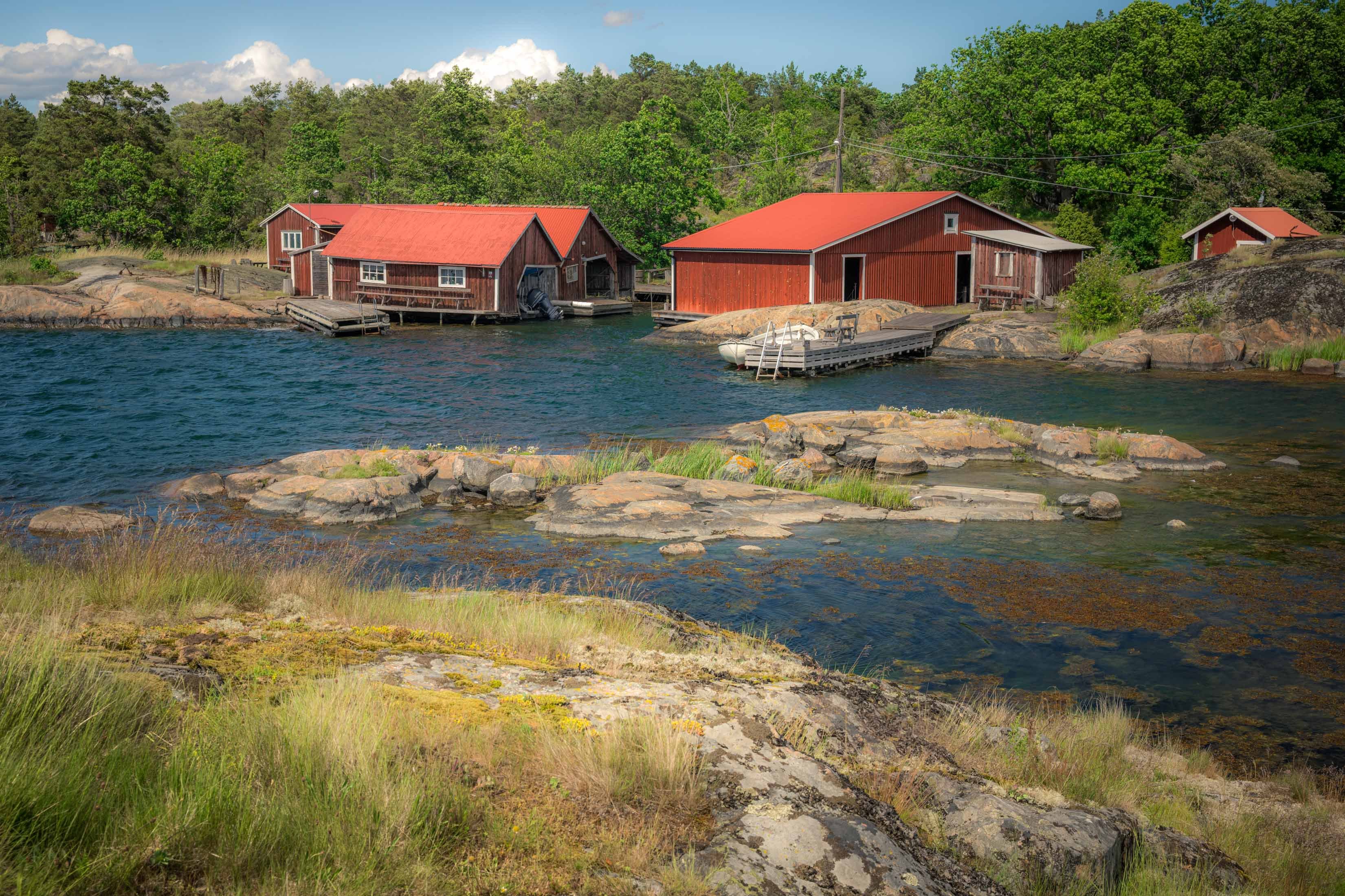 Rode Scandinavische bootloodsen met felrode daken op rotsachtige eilandjes, omgeven door turquoise water en groene bossen op een zomerse dag.