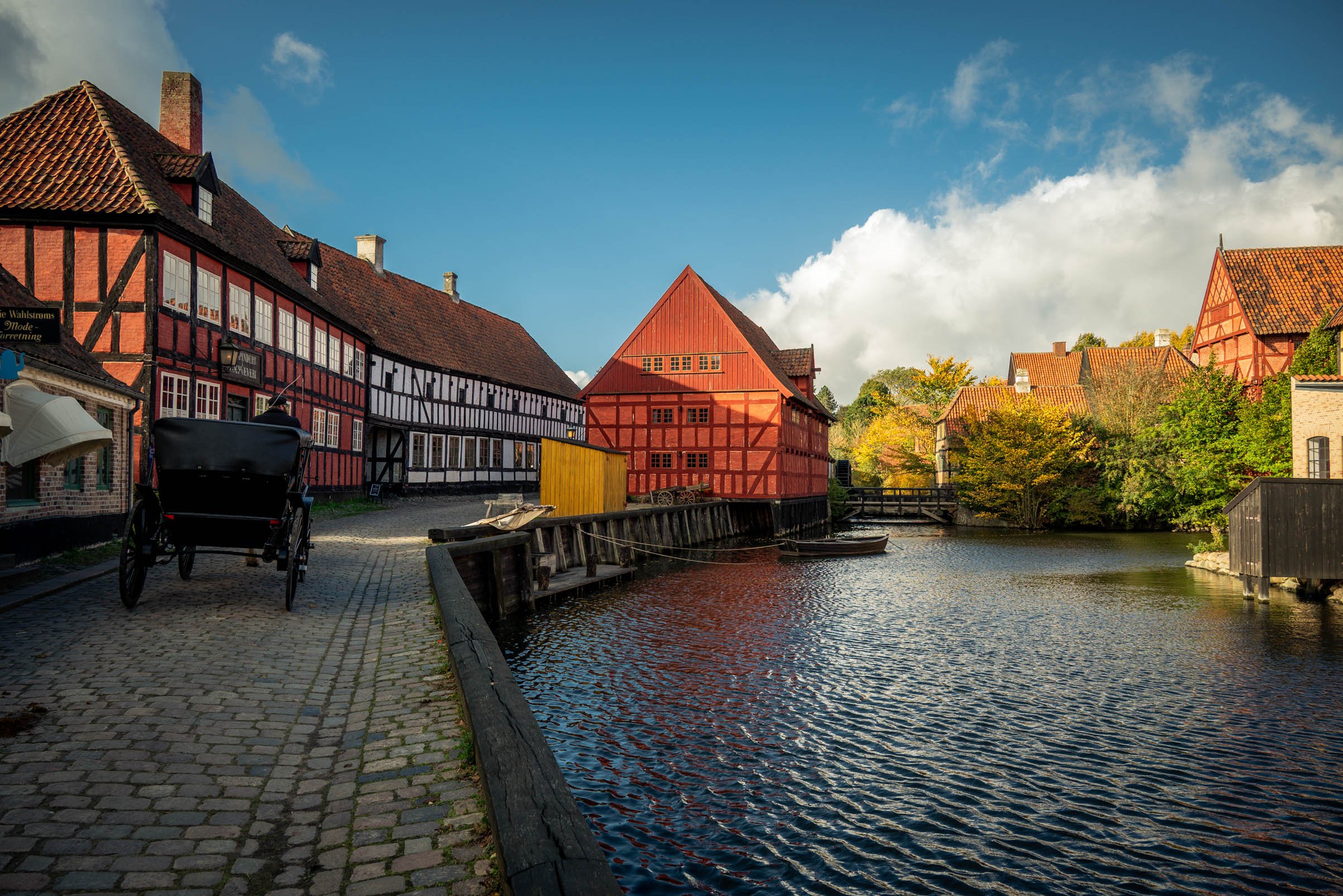 Historische Scandinavische havenstad met rode vakwerkhuizen langs een waterkanaal en een zwarte koets op een kinderkopjesplein.