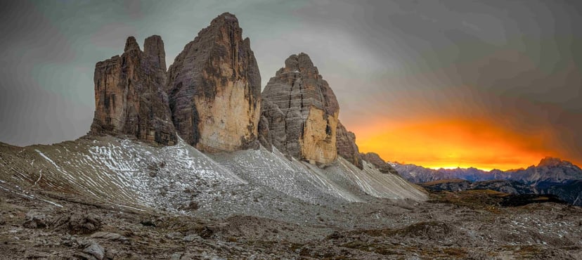 Tre Cime di Lavaredo rocky peaks at dramatic orange sunset, Dolomites.