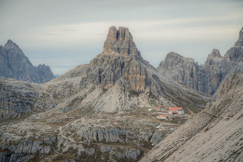 Mountain refuge with red roof beneath dramatic Dolomite peaks, Italy.