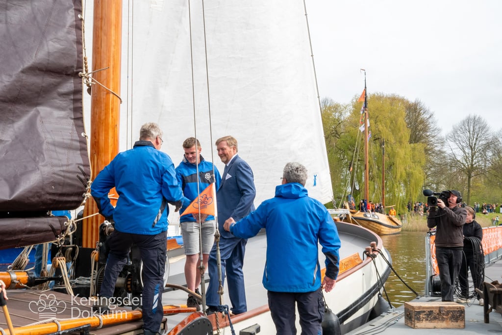 Man in blauw pak schudt handen met bemanning op een houten zeilboot tijdens Koningsdag in Dokkum.