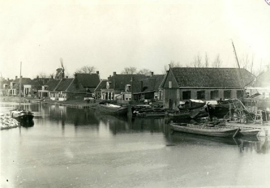Historic Dutch canal town with boats and windmill, black-and-white photo.
