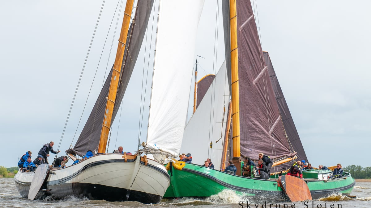 Drie traditionele houten zeilboten in een spannende race op Fries binnenwater met volle bruine en witte zeilen.