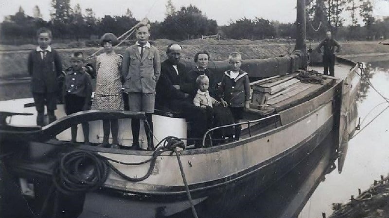 Zwart-witfoto van een gezin met vijf kinderen geposeerd op de boeg van een houten binnenvaartschip langs een kanaal, circa jaren twintig.